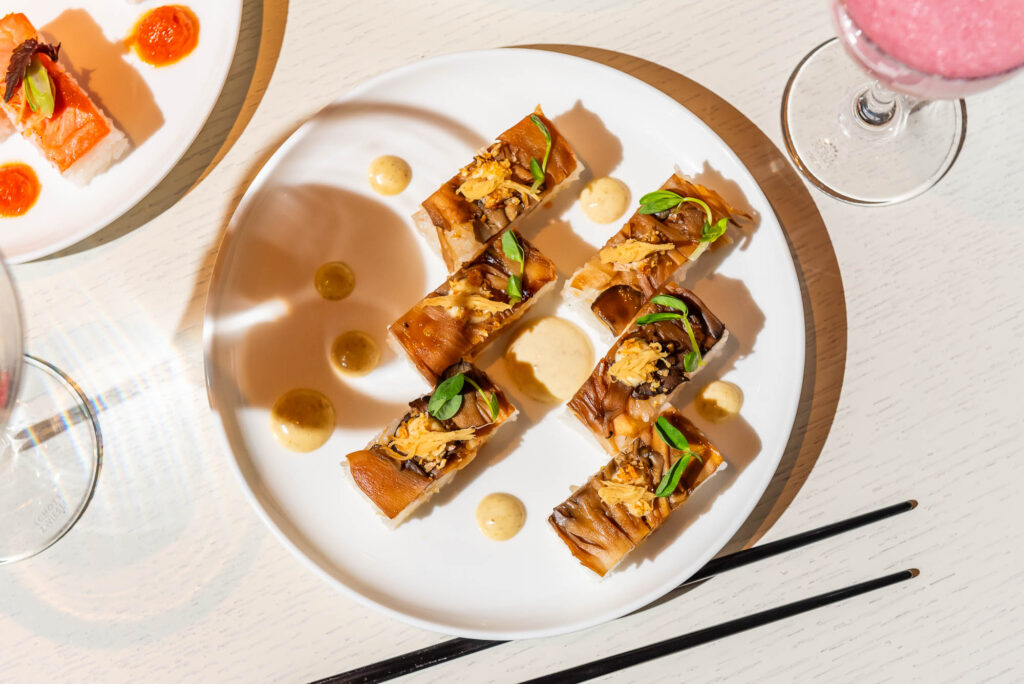 Sushi on a white plate against a light wood table with black chopsticks