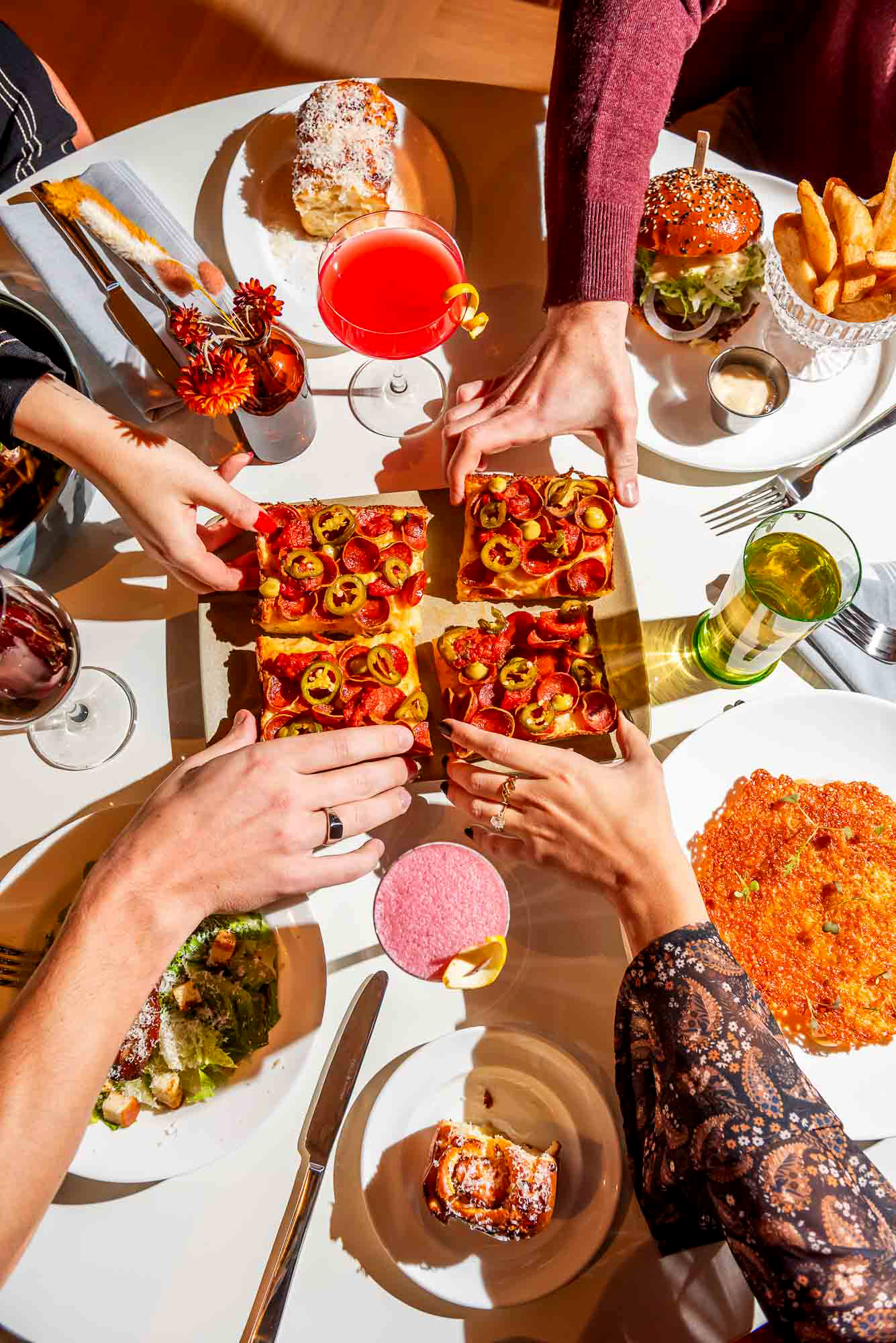 Hands reaching in to grab a slice of Detroit-style pizza at The Joneses restaurant in Toronto