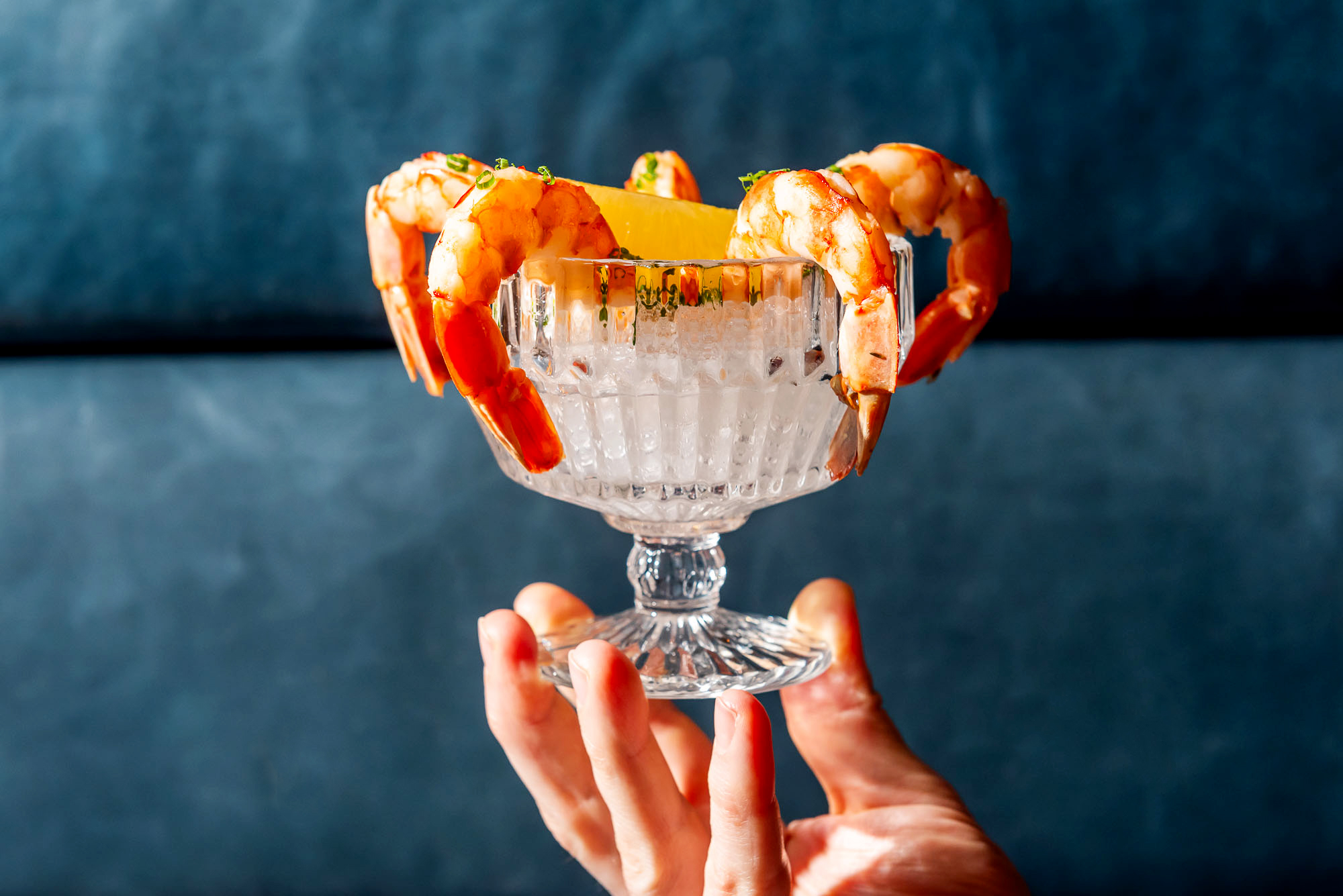 Hand holding a shrimp cocktail against a blue backdrop at The Joneses restaurant in Toronto