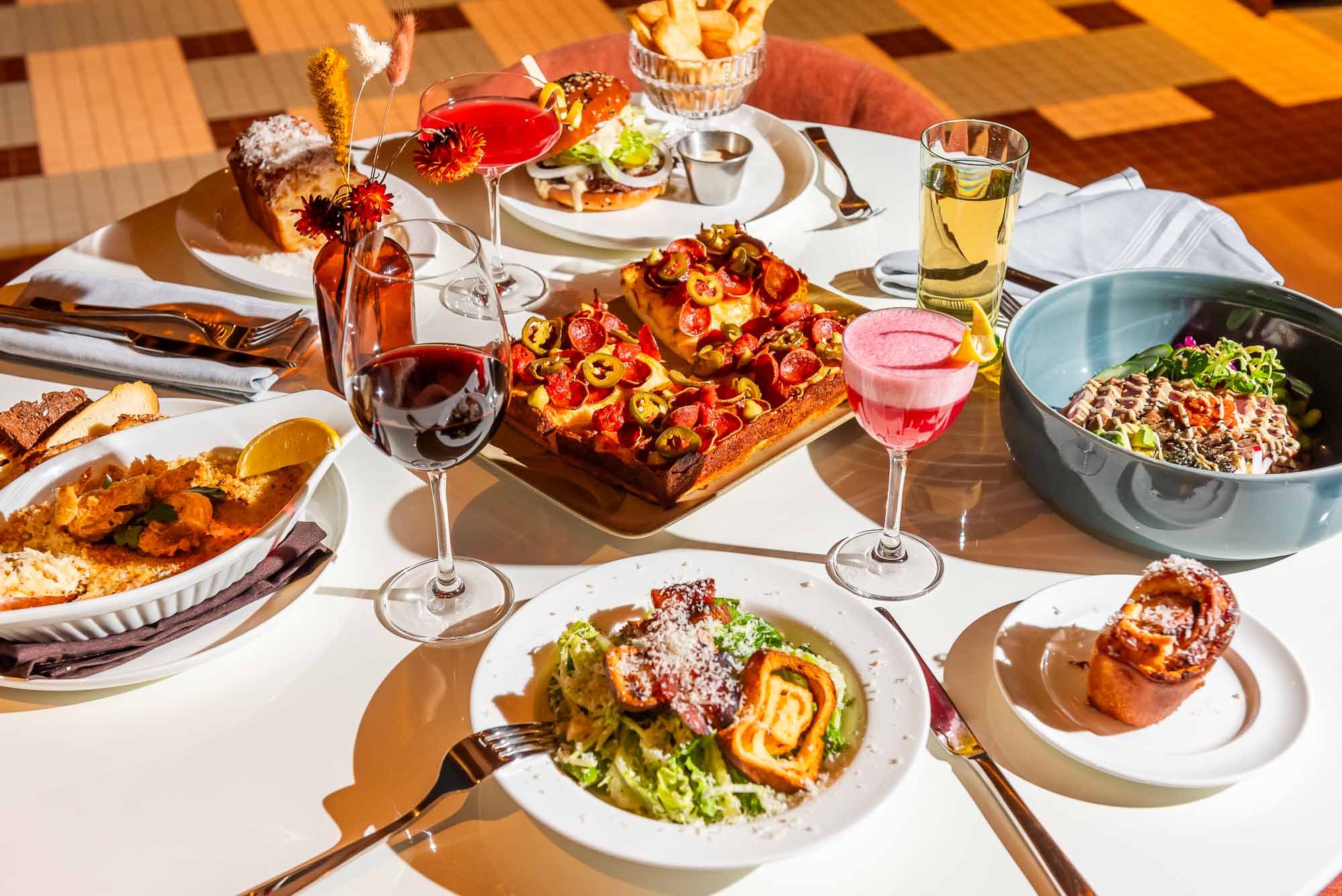 A variety of dinner entrees, cocktails and wine sitting on a white table top at The Joneses restaurant in Toronto