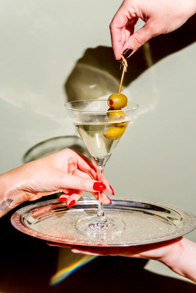 Two hands reaching for a martini on a silver platter at The Joneses restaurant in Toronto